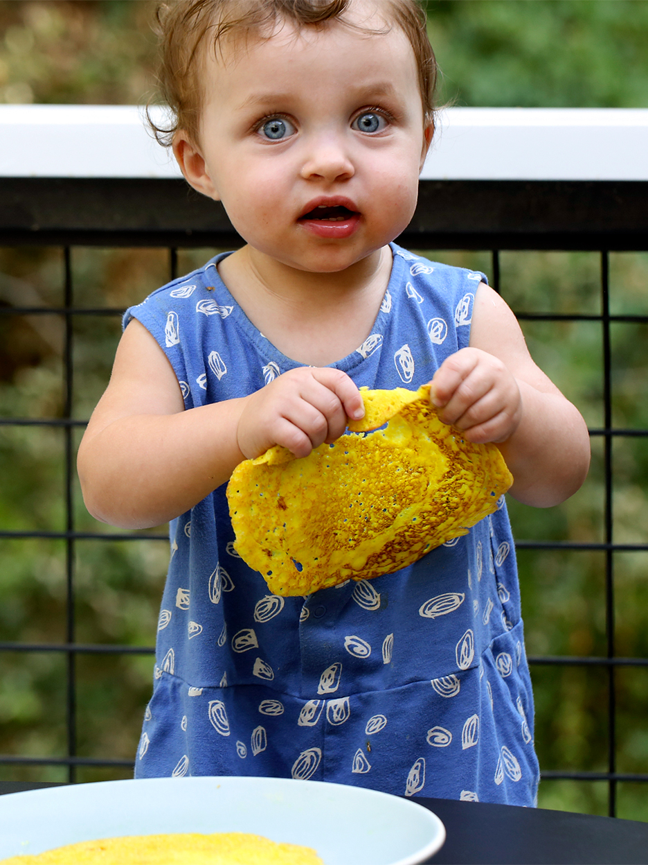 baby in blue dress holding dosa pancake